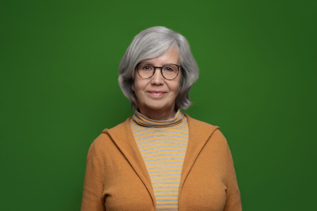 Eine lächelnde Frau mit einer Brille in einem orangem Oberteil vor einem grünem Hintergrund