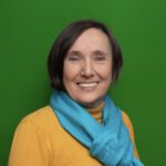 Eine lächelnde Frau in einem orangen Pullover mit einem blauen Schaal vor einem grünem Hintergrund